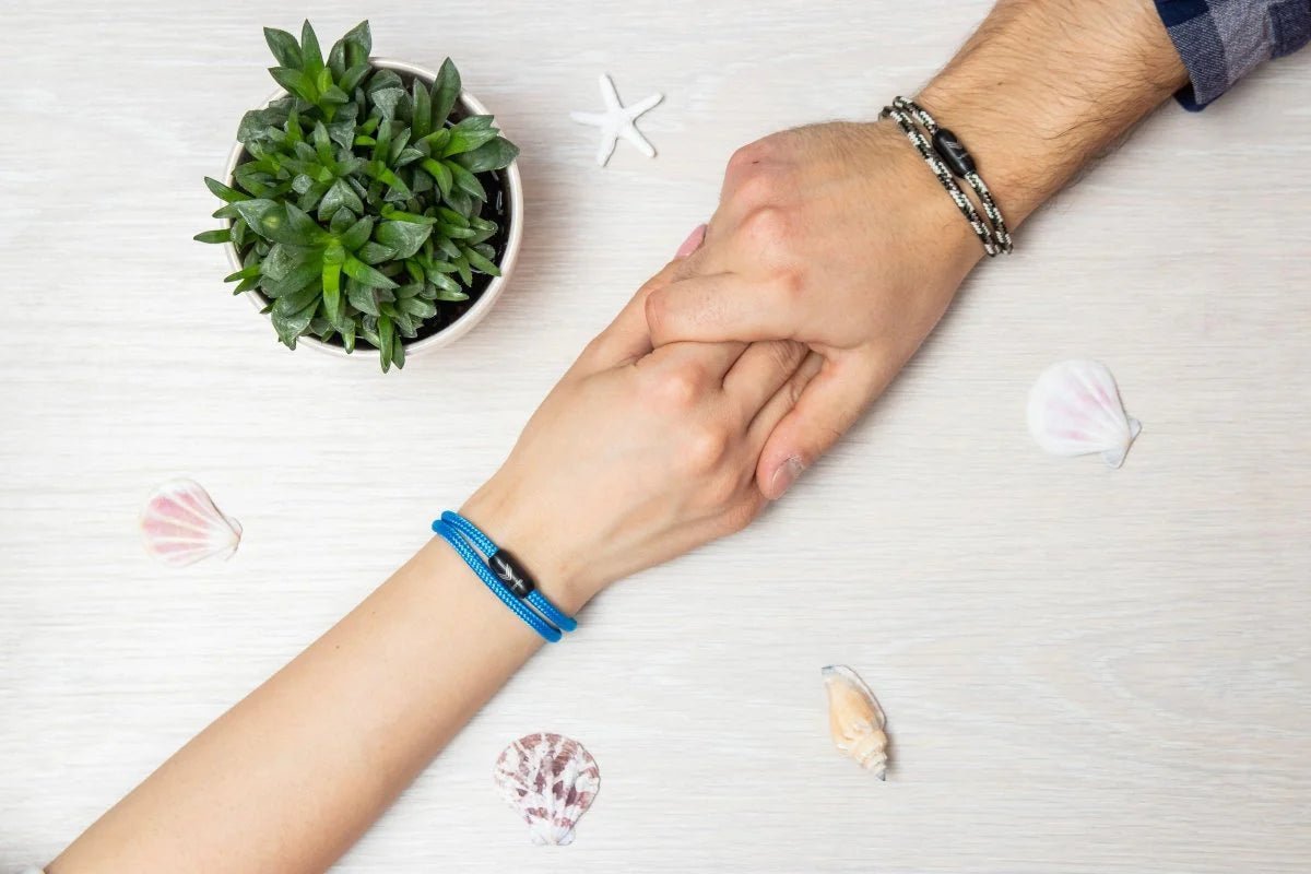 Vertig Magnetic Nautical Paracord Bracelet Blue on a woman&#39;s hand, holding a man&#39;s hand with a camo bracelet.