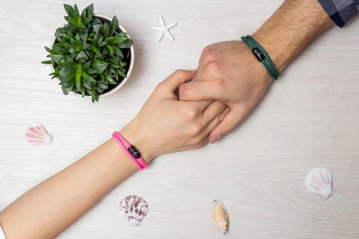 Vertig Magnetic Nautical Paracord Bracelet Pink on a woman&#39;s hand, holding a man&#39;s hand with the green bracelet.